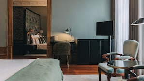 A hotel room with a large bed, two armchairs, a desk with a lamp, and a television. - Torel Royal Court (Guimarães)