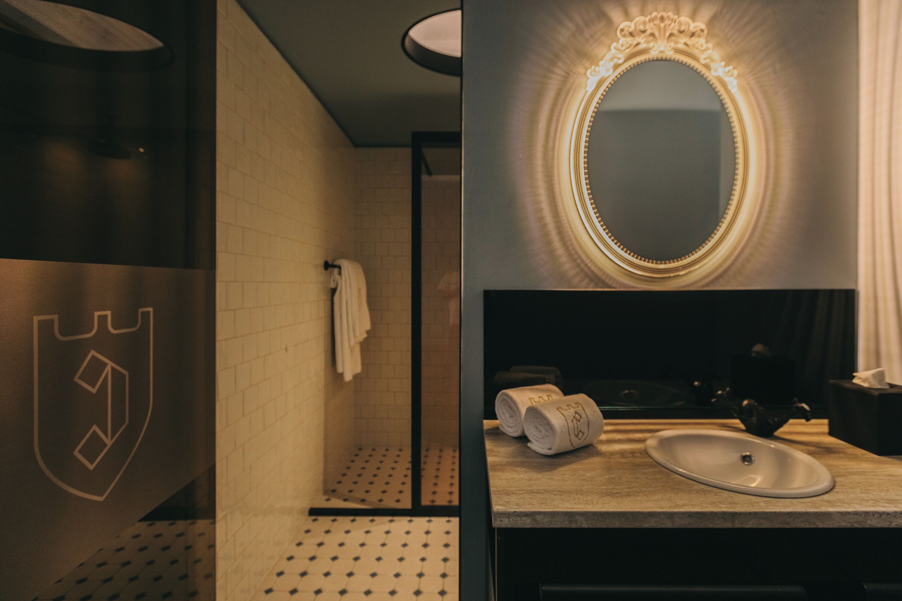 Un baño moderno con piso de baldosas, zona de ducha, lavamanos con espejo y toallas.