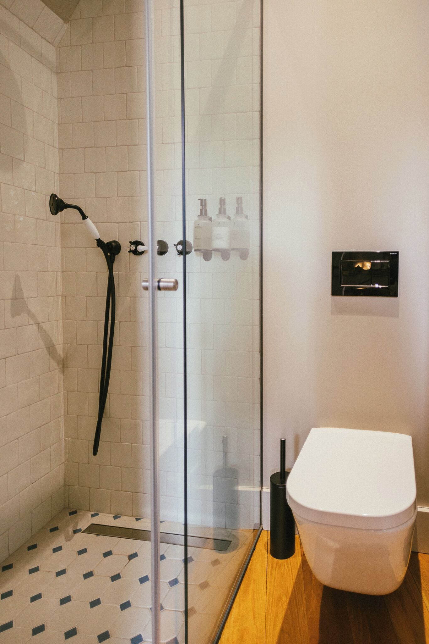A modern bathroom with a glass shower enclosure, a white toilet, and a black handheld showerhead.