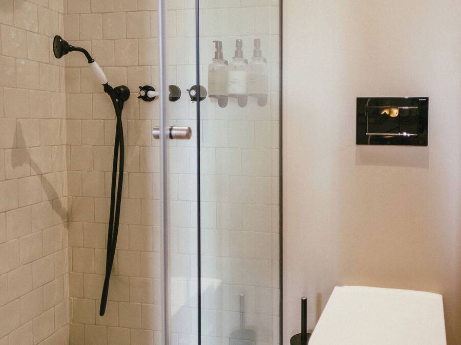A modern bathroom with a glass shower enclosure, a white toilet, and a black handheld showerhead.