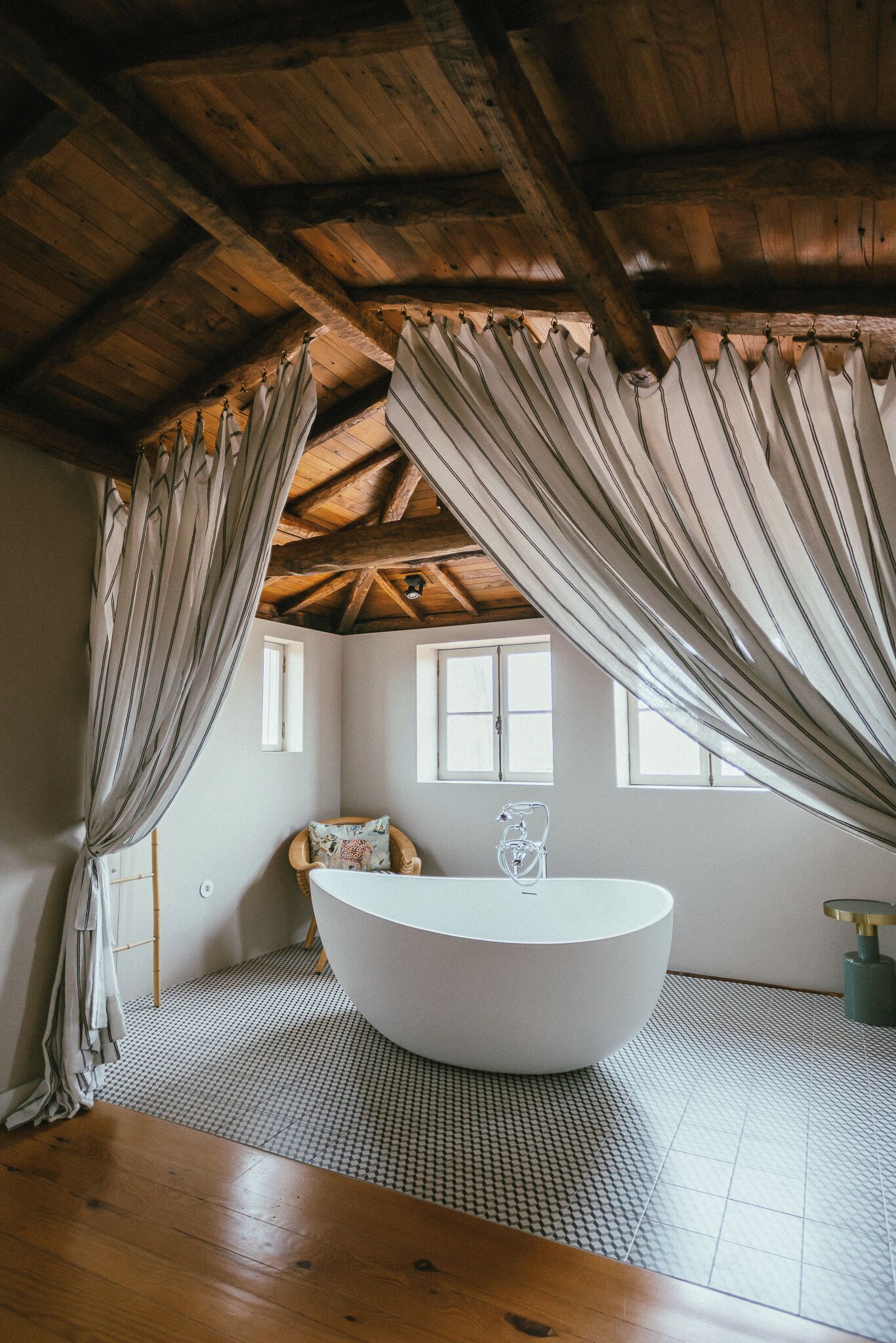 A room with a large bathtub, wooden ceiling beams, and a checkered floor.