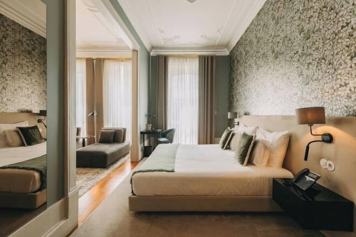A hotel room with a bed, a sofa, a desk, and a mirror.