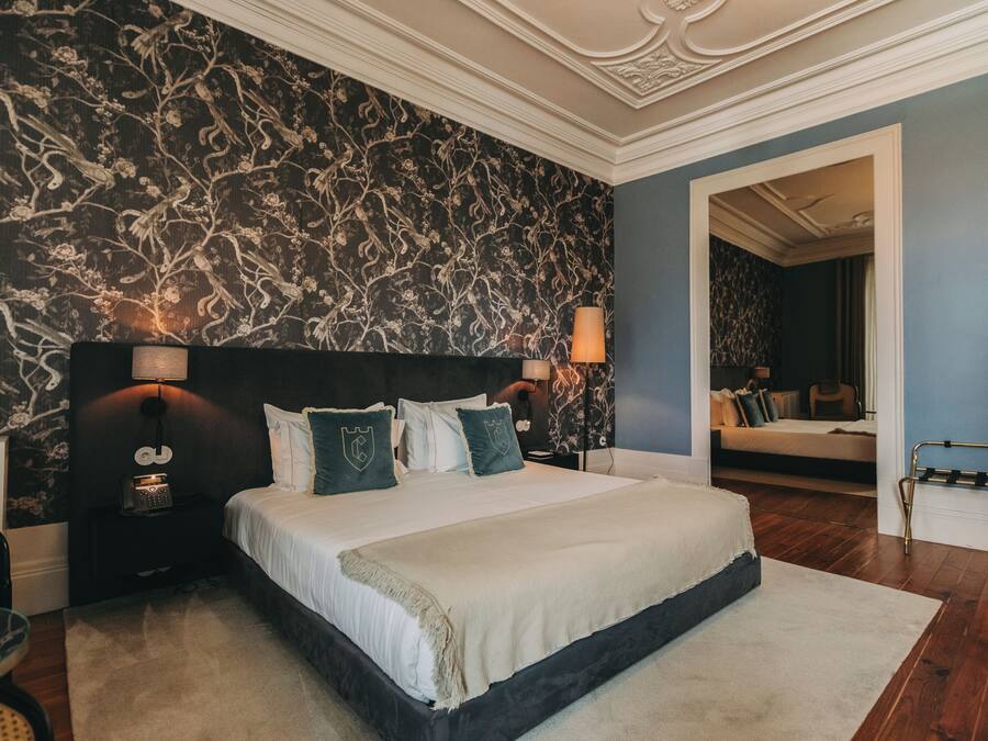 A bedroom with a large bed, dark patterned wallpaper, and a nightstand with a lamp.