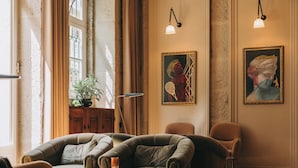 A cozy room with a leather sofa, a small table, and two chairs. There are framed artworks on the wall and a plant on a cabinet. - Torel Royal Court (Guimarães)