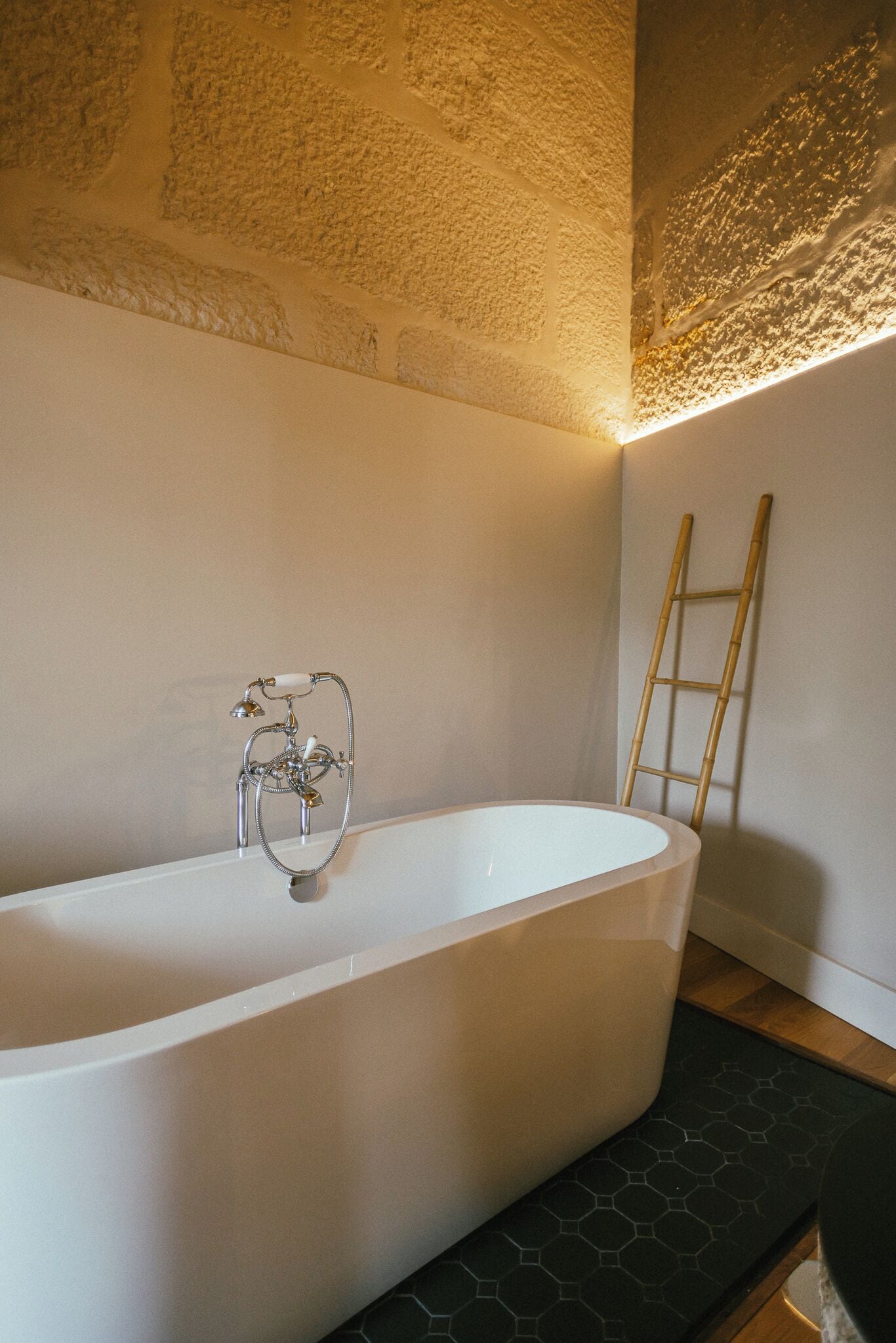 A modern bathroom with a freestanding bathtub, a wooden ladder, and a hexagonal patterned floor.