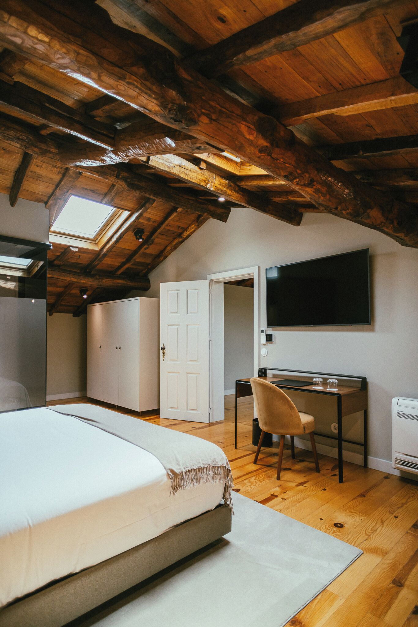 Un dormitorio con techo de madera, una cama, un escritorio y una silla.