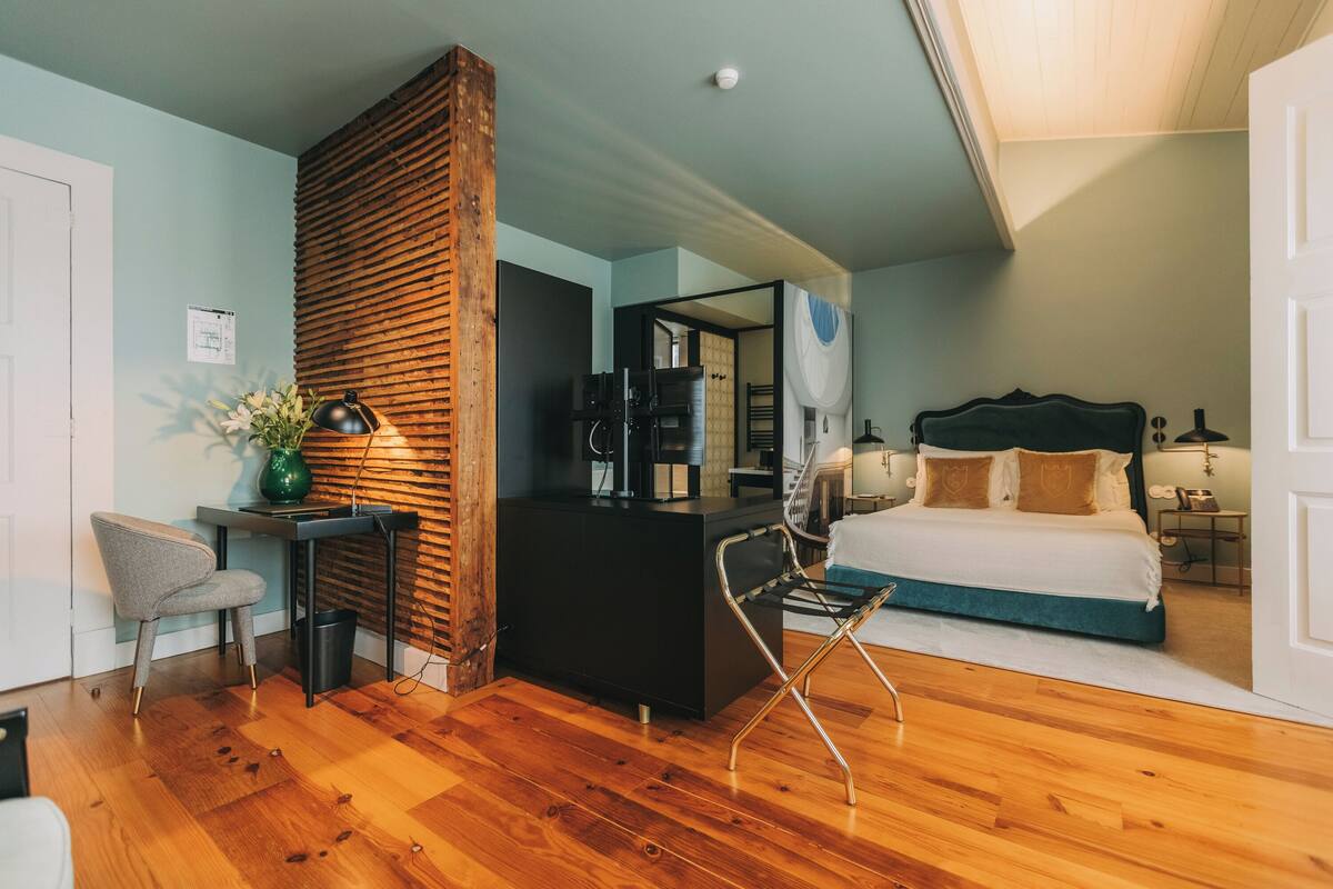 A modern bedroom with a wooden accent wall, a black desk, a chair, a bed with white and blue bedding, and a small side table.