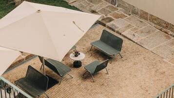 An outdoor patio with a table and four chairs, an umbrella, and a small round table with a vase.