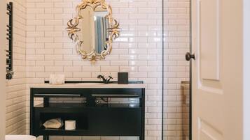 Une salle de bain avec des murs recouverts de carreaux blancs, un meuble-lavabo noir, un miroir avec un cadre doré et des toilettes blanches.