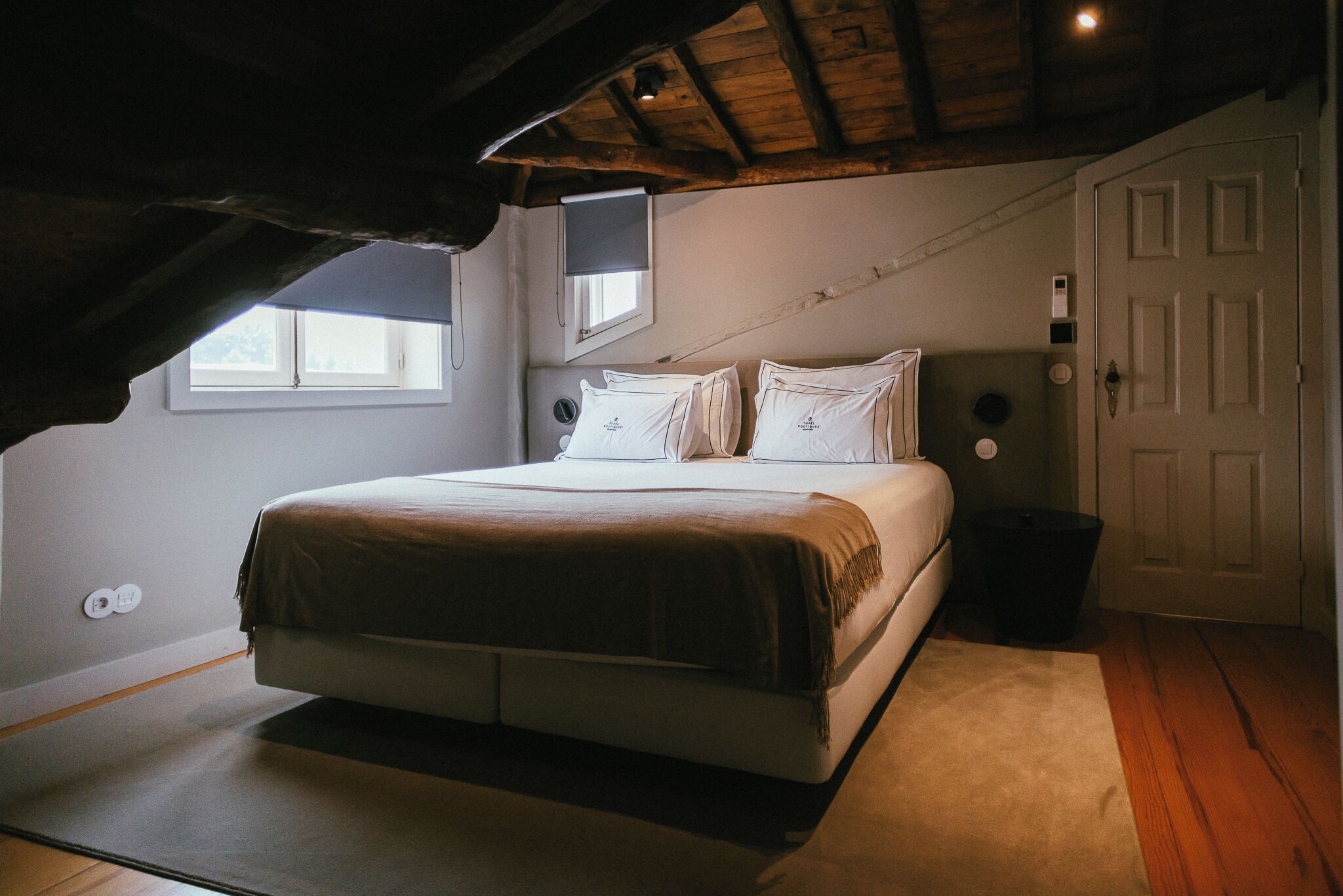 Ein Schlafzimmer mit einem Bett, einem Fenster, einer Tür und einer Decke mit sichtbaren Holzbalken.