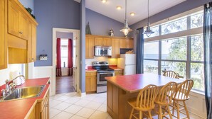 Una cocina con armarios de madera, un lavamanos de acero inoxidable, un microondas, un horno y una isla grande con sillas.