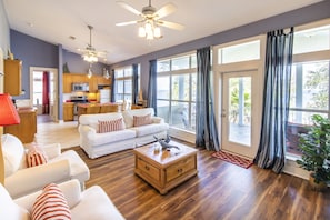 A spacious living room with a white sofa set, a wooden coffee table, and a ceiling fan.