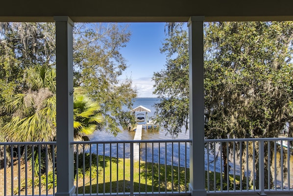 A view from a covered porch overlooking a body of water with a dock and a small building.