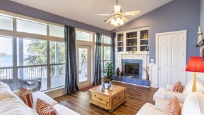 Un salón espacioso con chimenea, ventanas amplias y un ventilador de techo.