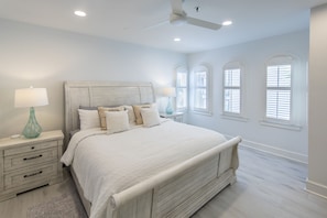 A bedroom with a large bed, white walls, and three windows with shutters.