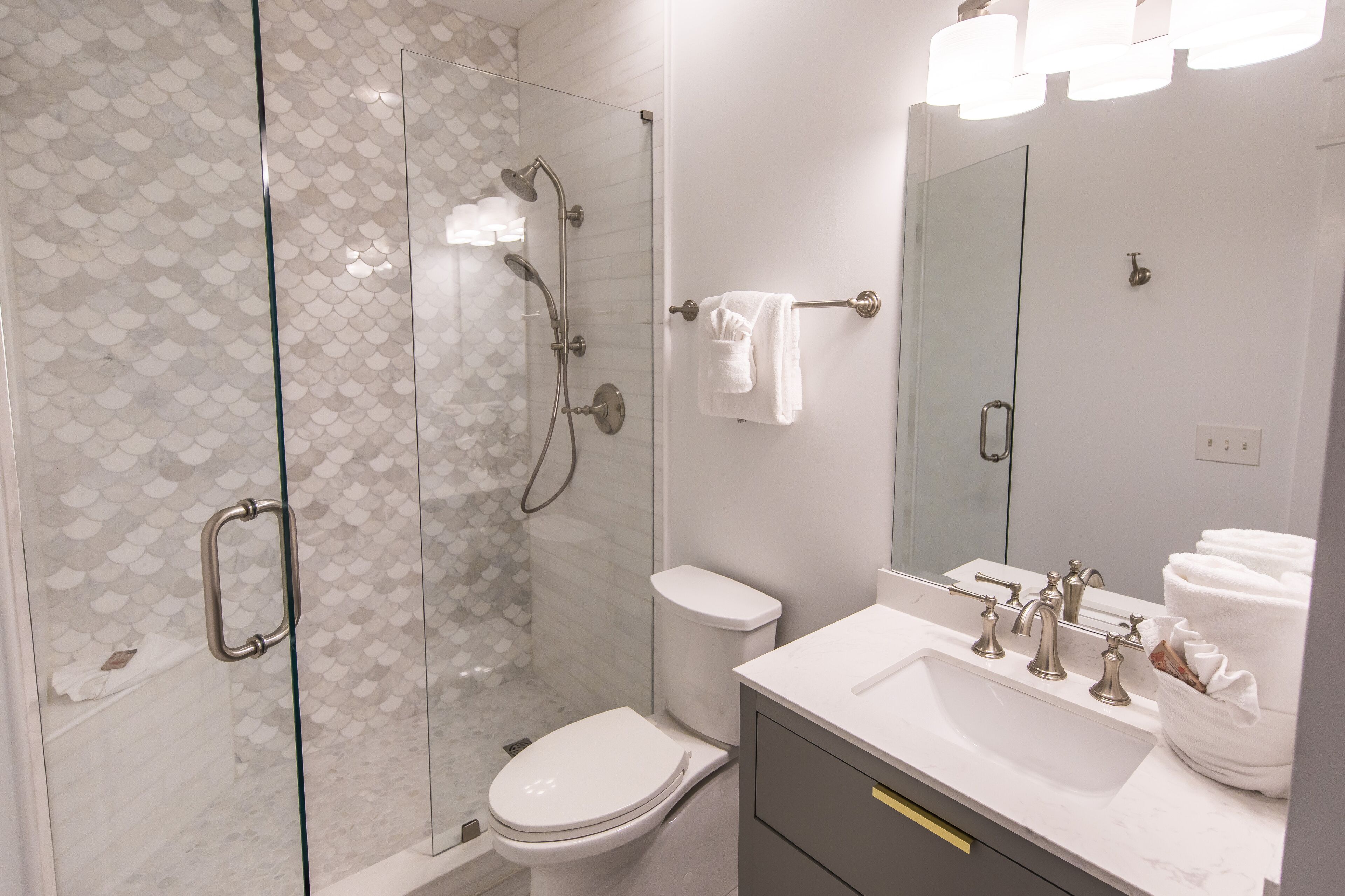 A modern bathroom with a glass-enclosed shower, a toilet, and a vanity with a sink and mirror.