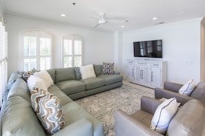 A living room with a sectional sofa, a patterned rug, and a flat-screen TV mounted on a cabinet.