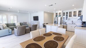 Un'ampia zona giorno con tavolo da pranzo, divani e una cucina con pensili bianchi e pannelli decorativi in piastrelle.