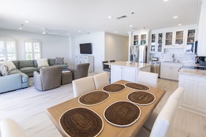 A spacious living area with a dining table, sofas, and a kitchen with white cabinets and a tiled backsplash.