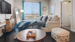 A modern bedroom with a bed, a sofa, a TV, a window with curtains, and a small table with a tray. -     Sip, Stay & Explore Traverse City Wine Country. Near all TC has to offer! (Traverse City)