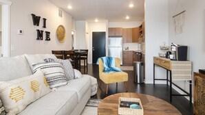 A modern living room with a sofa, coffee table, and a chair. There is a kitchen area in the background with wooden cabinets and a refrigerator. -     Sip, Stay & Explore Traverse City Wine Country. Near all TC has to offer! (Traverse City)