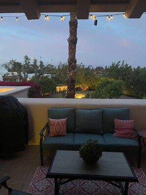 An outdoor seating area with a sofa and a table, string lights overhead, and a view of the landscape.