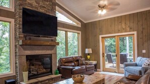 Una sala de estar con chimenea de piedra, sofás de cuero, un televisor de pantalla plana y un ventanal con vistas a una terraza.