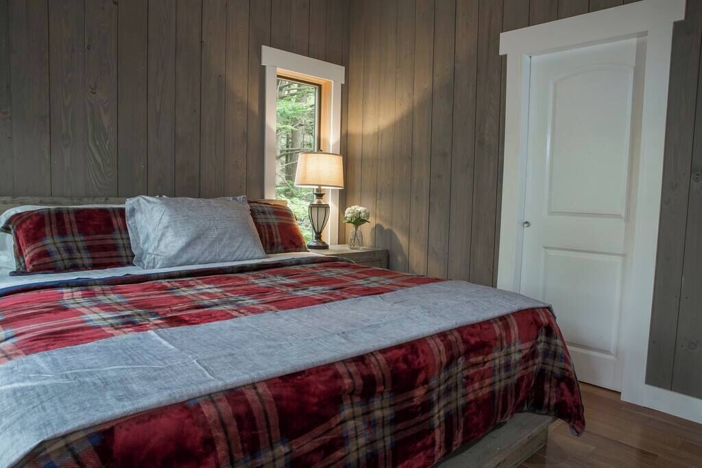 Un dormitorio con una cama, una mesita de noche, una lámpara y un ventanal.