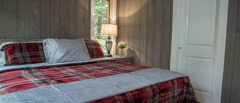 Un dormitorio con una cama, una mesita de noche, una lámpara y un ventanal.