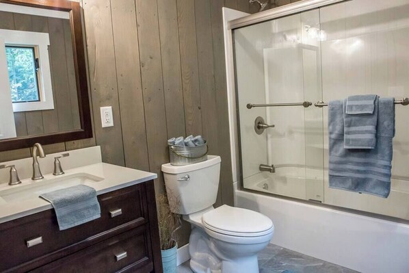 A bathroom with a wooden panel wall, a white sink with a towel, a toilet, and a glass-enclosed shower area.