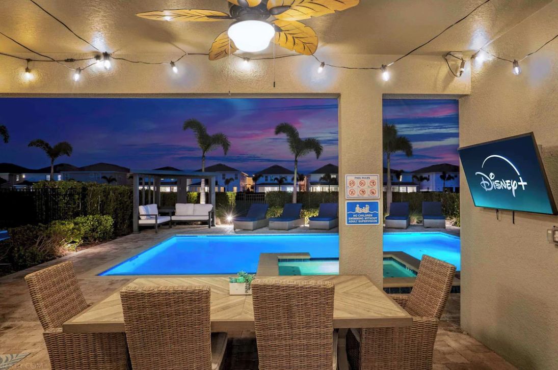 A poolside area with lounge chairs, a dining table, and a Disney+ sign.