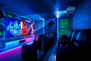 A home theater room with a large flat-screen TV, leather reclining chairs, and a projector.