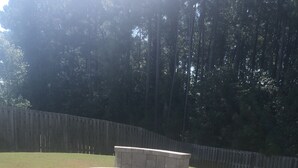 A circular stone fire pit surrounded by a brick patio, with a wooden fence and trees in the background. - Beautiful  5 bdrm, 3 bthrm, 15 minutes to the Masters (Grovetown)