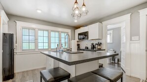 Una cocina moderna con una isla grande, armarios blancos y un refrigerador de acero inoxidable.