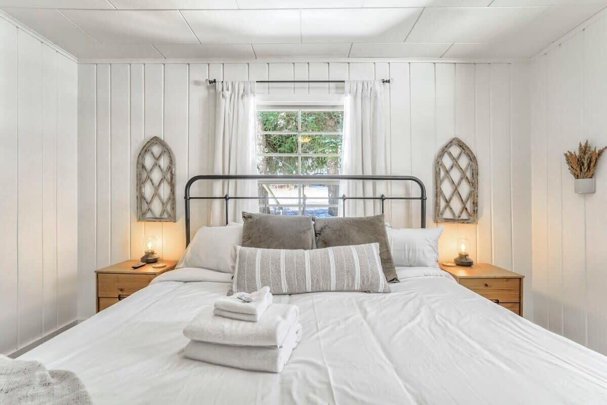Ein Schlafzimmer mit einem Bett, zwei Nachttischen, einem Fenster mit Vorhängen und dekorativen Wandleuchten.