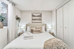 A bedroom with a large bed, bedside lamps, a wall-mounted artwork, and a window with curtains.