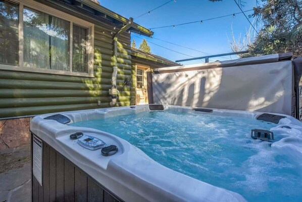 A hot tub with a wooden deck and a house in the background.