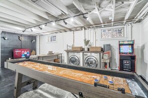 A laundry room with a foosball table, washing machines, and a Mortal Kombat arcade game.