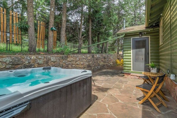A hot tub in a stone patio area with a wooden fence and trees in the background.