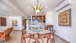 A dining area with a round glass table, wooden chairs, and a decorative chandelier. - Beach-Level Escape Featuring a New Private Plunge Pool and Ocean Views! (Akumal)