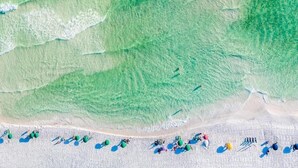 An aerial view of a beach with a sandy shore and a few scattered umbrellas.