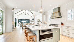 A modern kitchen with a central island, bar stools, stainless steel appliances, and a large window.