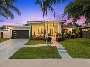 Une maison moderne avec un garage, une pelouse bien entretenue et une véranda aménagée avec du mobilier d’extérieur.