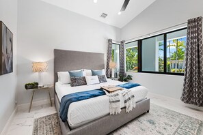 Une chambre moderne avec un grand lit, une table de chevet, une lampe et une vue sur la verdure.