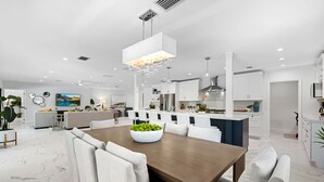 A modern kitchen with white cabinetry, a central island, and a dining area with a wooden table and white chairs.
