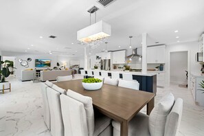 A modern kitchen with white cabinetry, a central island, and a dining area with a wooden table and white chairs. - Modern Heated Pool Getaway Near Las Olas, Dining & Beaches! (Fort Lauderdale)