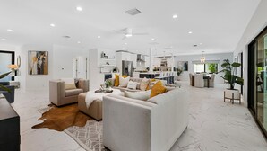 A modern living room with a sofa, a dining area, and a kitchen in the background.