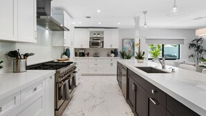 A modern kitchen with white cabinetry, stainless steel appliances, and a marble floor.