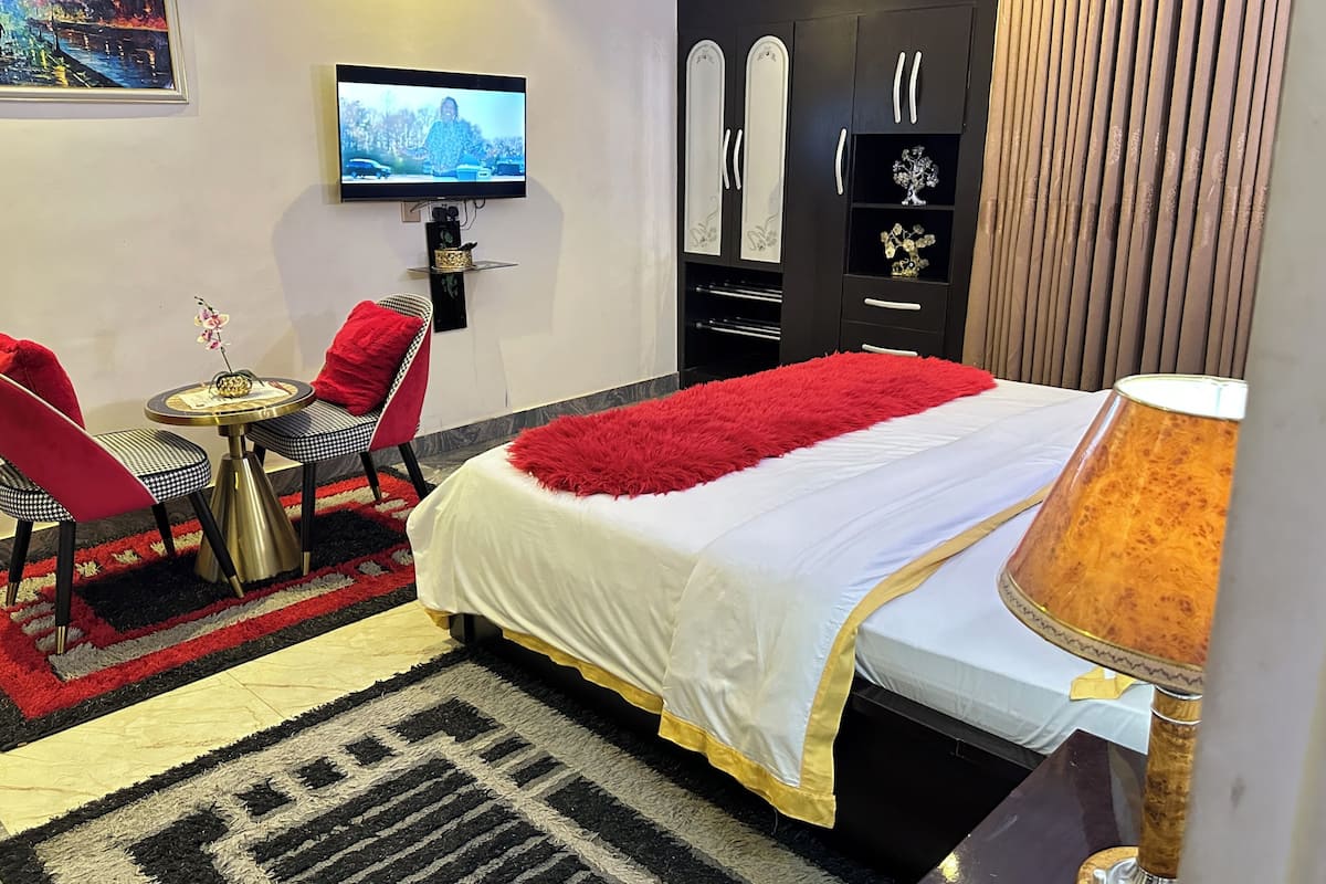Quarto de hotel com cama, televisão, secretária e um cadeirão, além de um guarda-roupa.