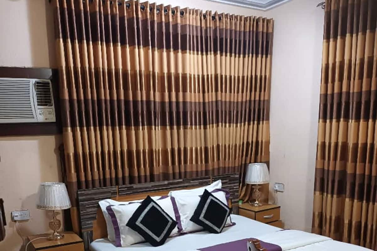 Quarto de hotel com uma cama grande, duas mesas de cabeceira, uma cadeira e cortinas.
